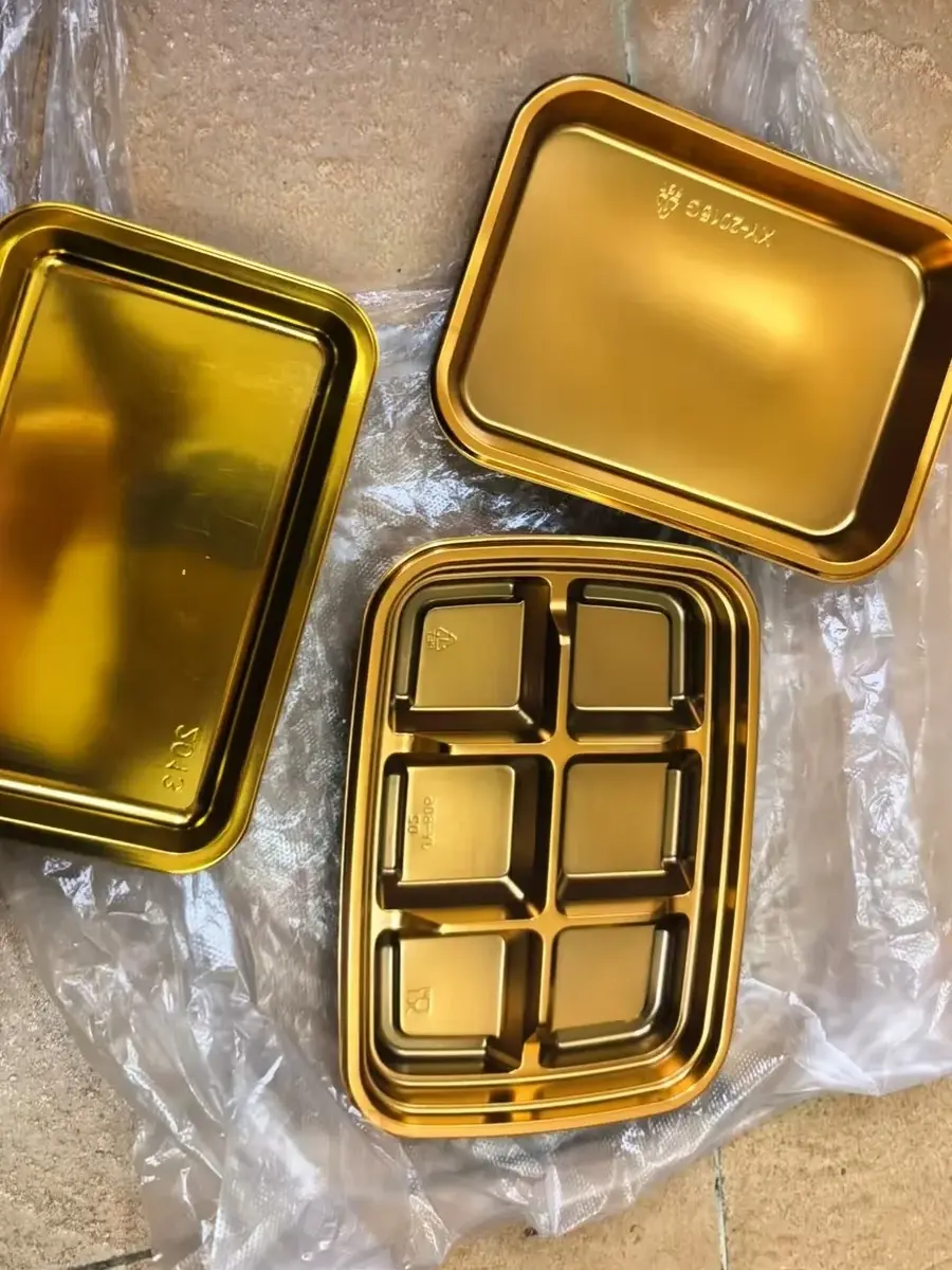 Gold thermoformed tray samples — six-compartment tray shown with single-cavity trays